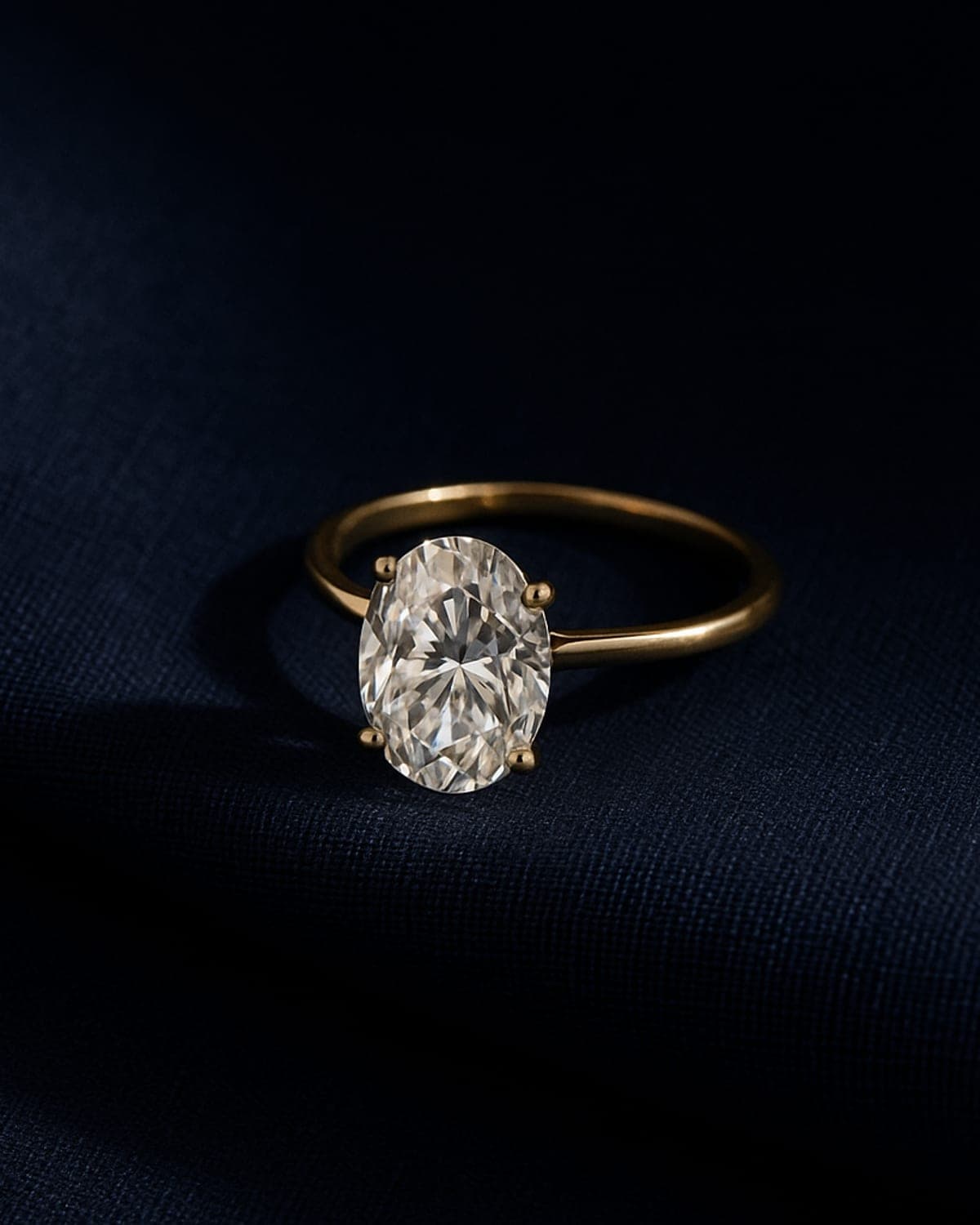 A large three-carat oval lab-grown diamond solitaire in yellow gold on a fine band