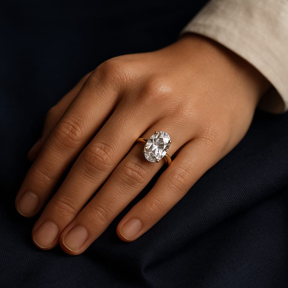A hand at rest wearing a large oval lab-grown diamond solitaire in yellow gold