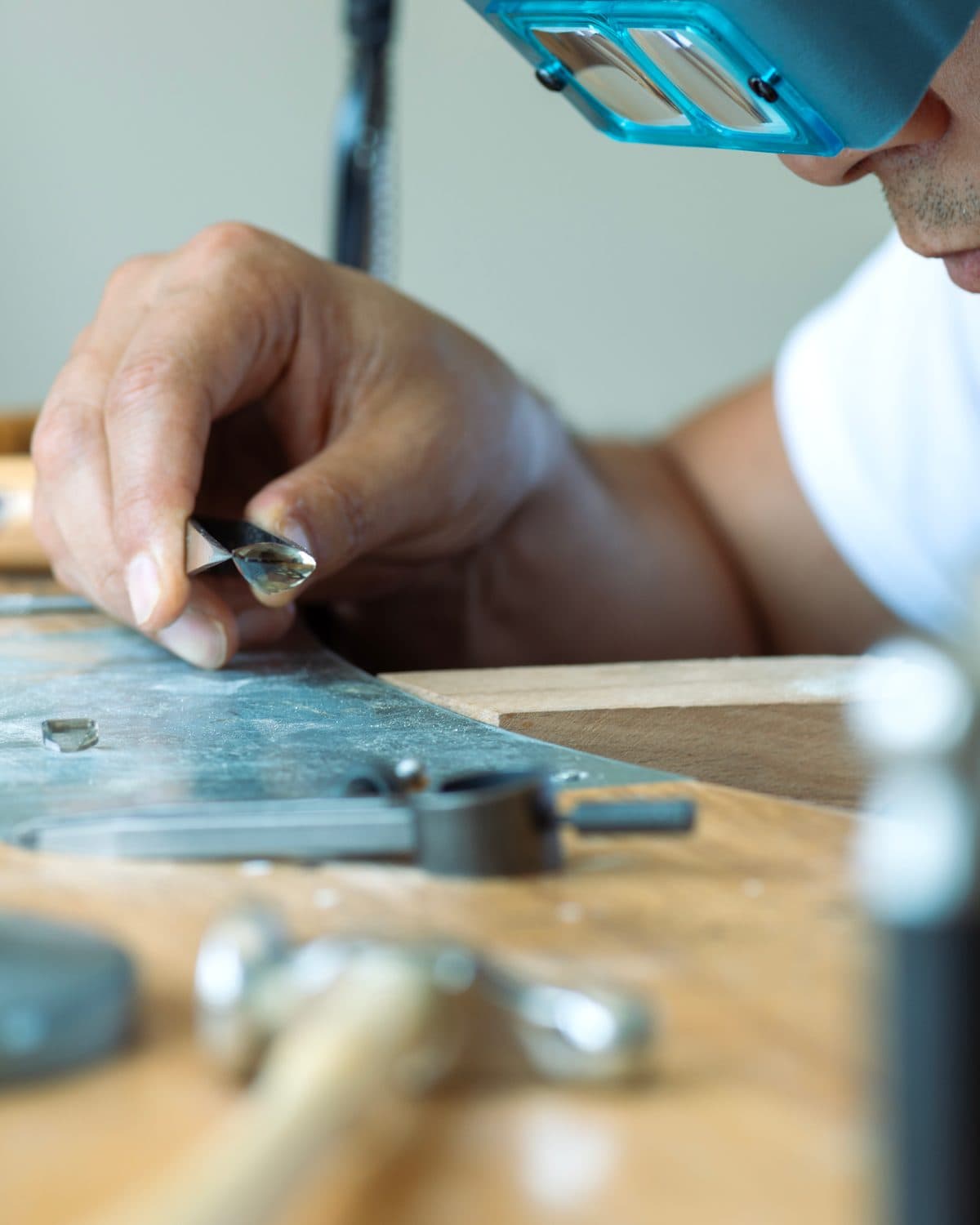 A jeweller wearing a loupe visor examining a loose lab-grown diamond held in tweezers at a workbench