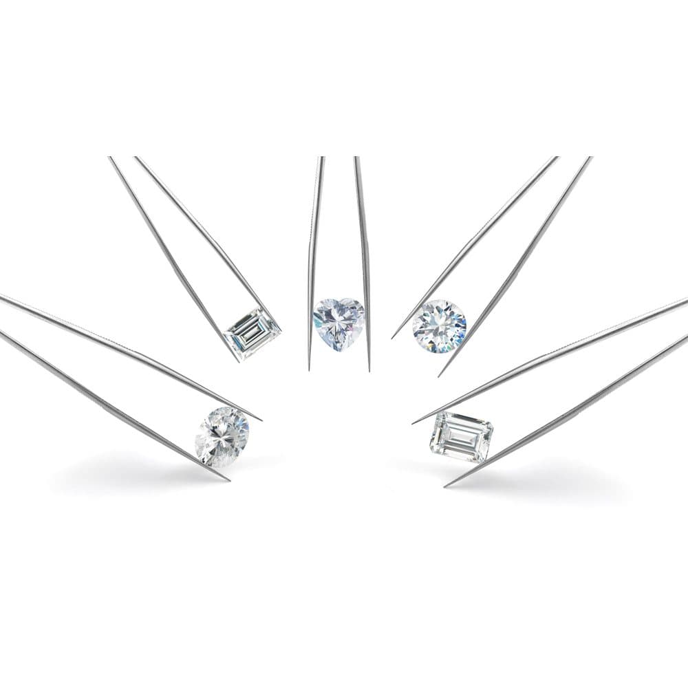 Five loose diamonds in different cuts — baguette, heart, round, oval and emerald — each held in jeweller's tweezers