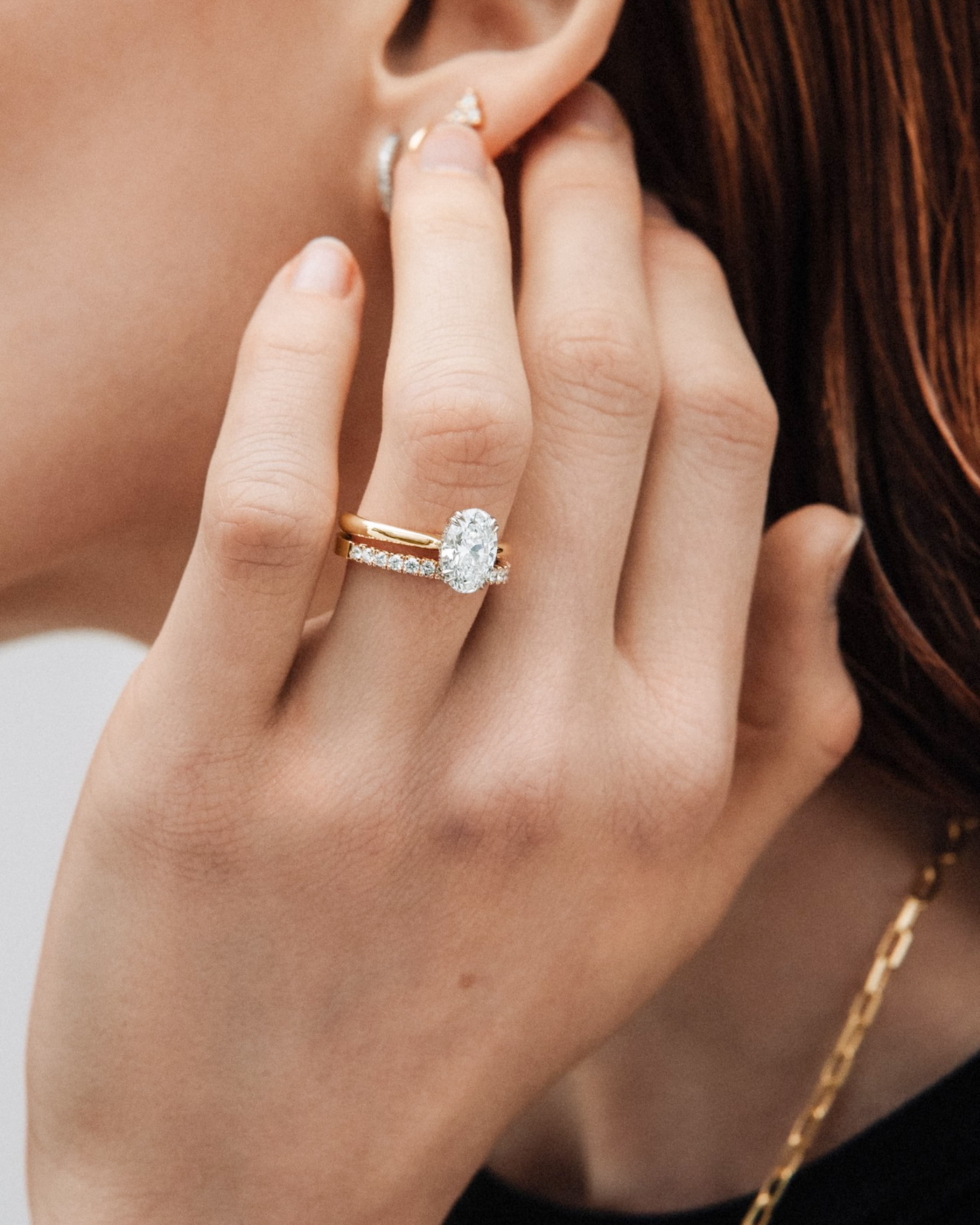 A yellow gold pear-cut diamond solitaire engagement ring with a pavé band on a dark background