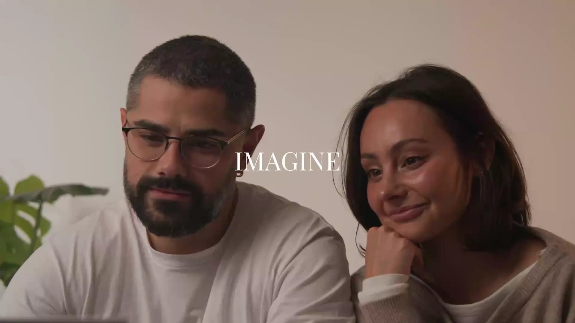 A couple smiling while reviewing an engagement ring design together on a laptop, with the word IMAGINE overlaid